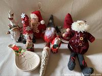 Seven small Santa and elf figurines of different designs and sizes, made from fabric and wood, displayed on a surface.