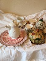 Set of plates, teapot, teacups, and decorative containers displayed on cloth background