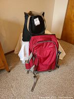 Photo showing the two bags: a red LL Bean suitcase sitting on the floor and a black Woods & Hyde shoulder bag with tan handles standing behind it