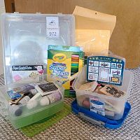 Overview photo showing plastic scrapbooking paper holder, Crayola marker box, plastic containers with craft stamps, inks, pens, and bubble mailers on carpeted floor.
