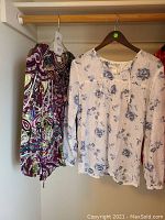 Photo of purple paisley patterned blouse and white blouse with blue floral print on wooden hangers.