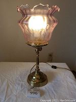 Brass lamp turned on showing illuminated pale lilac glass shade with Art Nouveau etching
