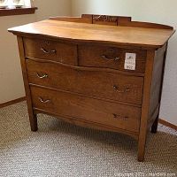 Full view of oak dresser showing four drawers with metal handles and sculpted backboard with carving.