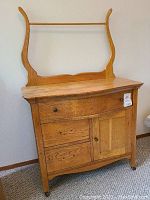 Front view of oak washstand showing curved backboard with towel bar, two drawers, and one door.
