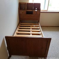 Full view of the twin oak bed frame with slatted base, three under-bed storage drawers, and the headboard with two small drawers and cubby holes.