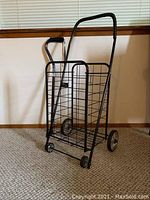 Full view of the black wire folding shopping cart standing upright on wheels.