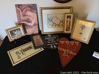 Nine assorted decorative wall art pieces and signs laid on black fabric.