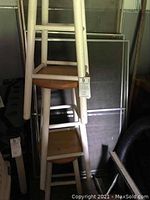 Photo showing four wooden barstools stacked, white painted legs with round wood seats in shed environment, some wear and dirt visible