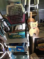 Overview image of kennel cab carrier atop shelving with Litter Maid boxes below, and wooden cat dish holder on top of boxes.