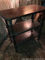 Angled view of the three-tier dark wood shelf showing turned legs and worn top surface