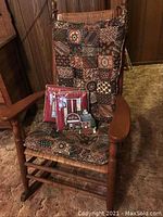 Close-up side view of vintage wooden rocking chair with patchwork cushion, showing wood detail and curved armrest.