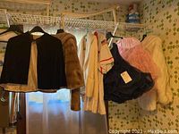 Hanging black velvet caplet, brown faux fur jacket, light-colored Awana shirt and navy and pink crinoline skirts hanging on a wire shelf