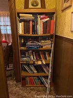 Wooden bookshelf filled with assorted books, mostly hardcovers and paperbacks, visible dust and wear