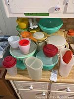 Overview of assorted Tupperware plastic containers, bowls, cups, and lids on kitchen counter needing cleaning.