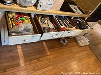 Three kitchen drawers pulled out showcasing an assortment of kitchen flatware and utensils, including forks, spoons, knives, and various cooking tools.
