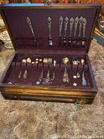 Wooden chest containing Oneida Community flatware on purple felt lining, showing entire set with utensils slotted inside chest.