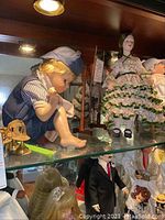 Shirley Temple doll, toddler boy doll in sailor outfit, and girl doll in ruffled dress displayed on glass shelf