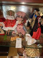 Full display of dolls including Square Dance Barbie style doll, Brian doll with train, Spain dancer doll, and baby doll arranged in glass cabinet.