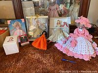 Three boxed Barbies, one Barbie doll in pink/white crochet dress with hat, small doll in orange crochet dress, all on carpet.