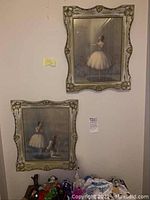 Photo of two framed ballerina artworks hanging on wall, with cream and gold ornate frames, showing the overall lot condition and setting