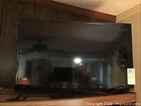 Front view of Insignia flat screen TV displaying black screen reflecting ceiling light and room.