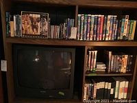 Full view of four shelves filled with DVDs and VHS tapes, with a large box set and a TV below the shelves.