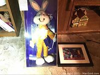 Photo showing Bugs Bunny 50th birthday limited edition doll in original display box standing next to framed cel on floor.