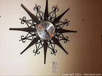 Large Mid-Century Modern sunburst style wall clock with metal and wood elements and silver face with black numbers and hands, labeled Welty.