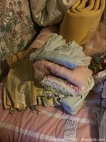 Stack of assorted pastel-colored vintage nightgowns and other sleepwear on a bed with pink striped bedspread.