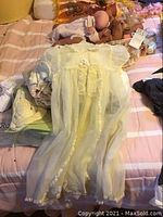 Vintage yellow Christening gown displayed on bed with sheer fabric and lace trim visible.