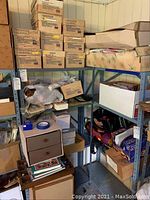 Metal shelving unit with multiple stacked cardboard boxes labeled for dollhouse miniature crafting supplies, some open boxes showing contents.