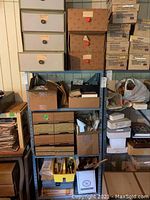 Full shelf showing cardboard boxes, small drawer cabinets, and bins filled with various miniature furniture and dollhouse supplies