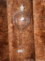Clear glass Pyrex separatory funnel with stopper and control valve laid on carpet.