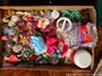 Close-up photo showing a box filled with numerous colorful costume jewelry pieces, including earrings, pins, and other small accessories.