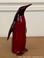 Front view of flambe-glazed porcelain penguin figurine showing red body and brown wings.