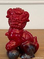 Front angle showing full body of the red veined Foo Lion ceramic figurine with one paw on a ball.