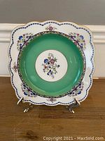 Full view of the square porcelain plate with a green center band and floral designs on white scalloped edges
