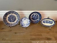 Four antique blue and white dishes on display from large Alma England plate to smaller dishes, showing detailed blue patterns and scenes.
