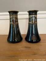 Pair of tall antique Royal Doulton vases shown side by side on wooden surface against light background.