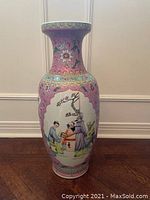 Full view of the large Chinese porcelain vase standing on floor against wall. Pink background with painted panels of traditional scenes.