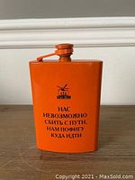 Front view of orange metal flask with Russian writing and expedition logo