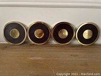 Four heavy brass coasters shown side by side with circular polished brass edges and centers, and textured dark brown material in the middle area.