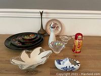 Various home decor pieces on table including plates, glass items, figurine, and dish.