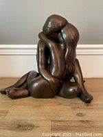 Full frontal view of bronze-plated sculpture showing two figures seated and entwined.