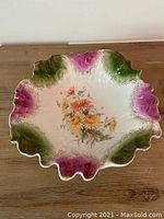 Full view of the decorative bowl showing scalloped edges with green and purple accents and central floral design.