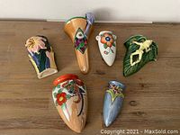 Set of six ceramic wall sconces displayed on a wooden surface, showing various shapes, sizes, colors, and designs including flowers and birds.
