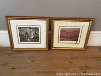 Two framed prints displayed side by side on a wooden floor, ornate gold frames, matted artwork.