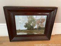 Frontal view of the oil painting in its dark wooden frame showing the entire work with some reflections on the glass surface.