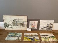 Group photo showing all six watercolor paintings arranged on floor, including a large barn scene, a small framed still life, and four landscape paintings.
