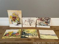 Overview of all six watercolor paintings arranged on the floor against a wall, showing variety of subjects including floral and landscape scenes.